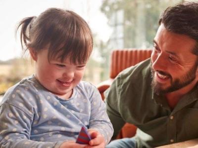 Man smiles and talks to a young girl who is playing with a toy